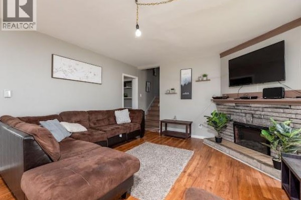 Living room featuring a large sectional sofa, a stone fireplace with a television above, and hardwood floors. - 86-88 Somerset, Moncton