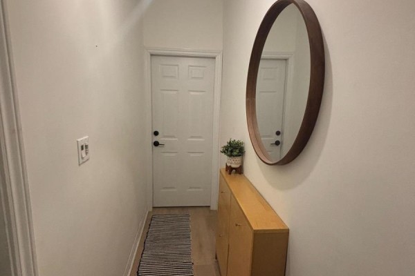 Narrow hallway with white door, wooden console table, and round mirror. - 86 Carlaw Avenue, Toronto