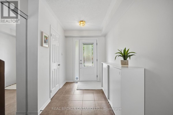 Interior hallway of a townhouse with beige tiled floors, white walls, and a white shoe cabinet. - 86 Coleridge Drive, Newmarket