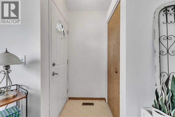 Interior entryway with a white front door, beige floor tiles, and a wooden closet door. - 86 Coventry Lane Ne, Calgary