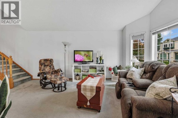 Living room with beige carpet, a brown recliner, a white media unit, and a sectional sofa. - 86 Coventry Lane Ne, Calgary