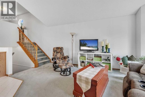 Living room with carpeted stairs, a floral recliner, and a brown sofa with bay windows. - 86 Coventry Lane Ne, Calgary