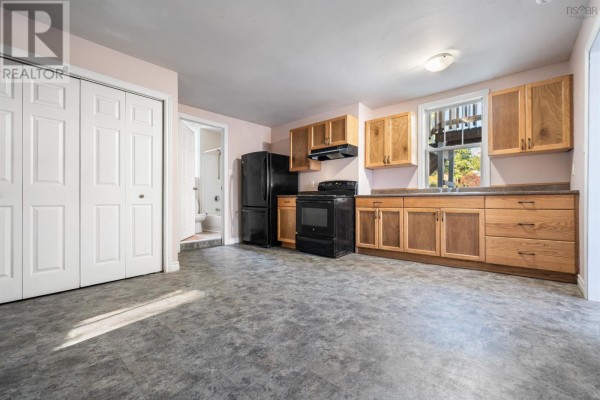 Kitchen with light pink walls, wood cabinets, black appliances, and a white bi-fold closet door. - 86 Denoon Street, Pictou