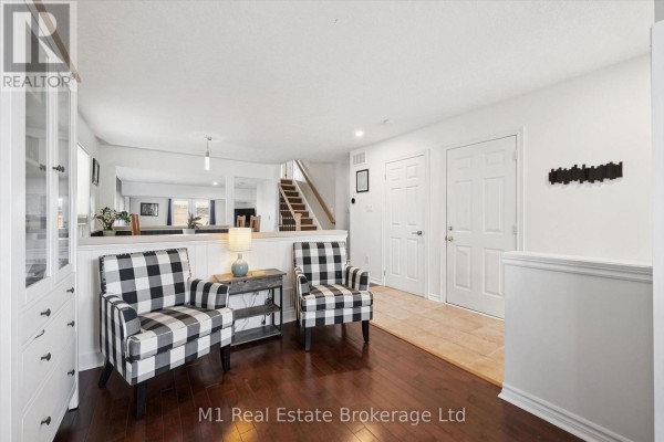 Interior view of a hallway and living area with dark wood floors, white walls, and black and white checkered armchairs. - 86 Milligan Street, Centre Wellington