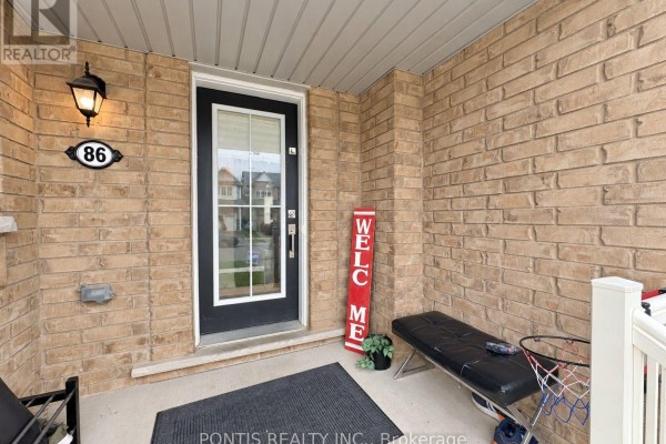Covered front porch with a black door, beige brick, and a small bench. - 86 Munro Circle, Brantford