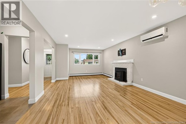 Living room with light grey walls, hardwood floors, white brick fireplace, and large window. - 86 Poirier Drive, Moncton