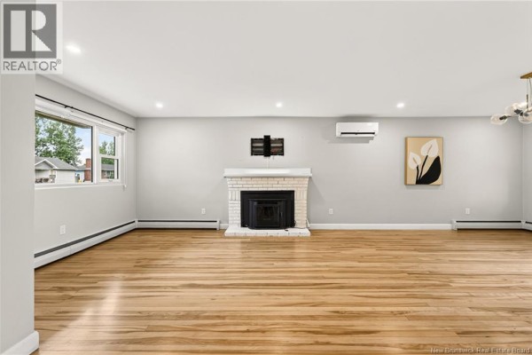 Spacious living room with hardwood floors, white brick fireplace, and air conditioning unit. - 86 Poirier Drive, Moncton