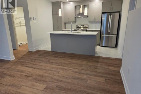 Open concept living area with kitchen island, grey cabinets, stainless steel appliances, and laminate flooring. - 86 Rutile Street, Clarence Rockland