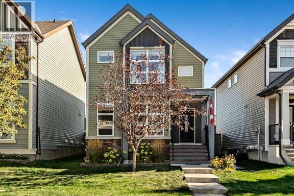 Front exterior of a two-story house with green siding, dark metal accents, and stone details. - 86 Walden Crescent Se, Calgary