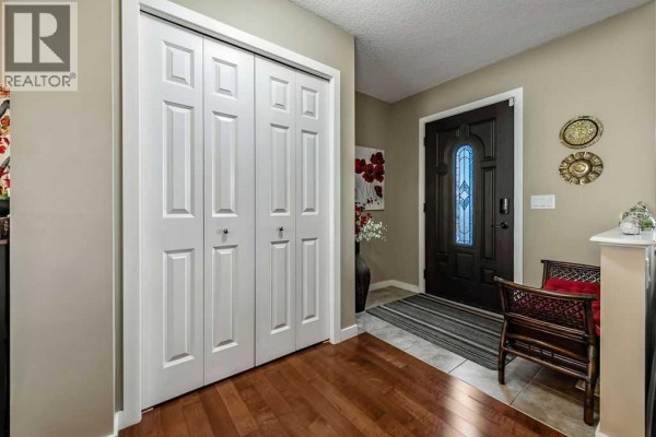 Interior entryway with a dark wood front door, tiled floor, and white bi-fold closet doors. - 86 Walden Crescent Se, Calgary