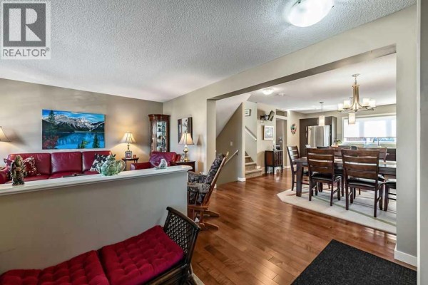 Open-concept living and dining room with hardwood floors, red sofas, and a wooden dining set. - 86 Walden Crescent Se, Calgary