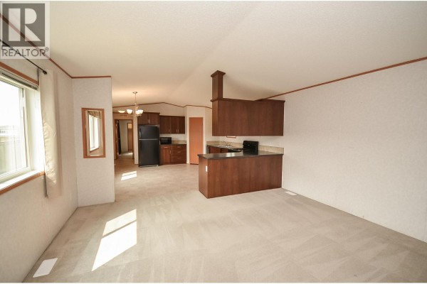 Open concept living and kitchen area with light carpet, dark wood cabinets, and black appliances. - 8608 79a Street, Fort St  John