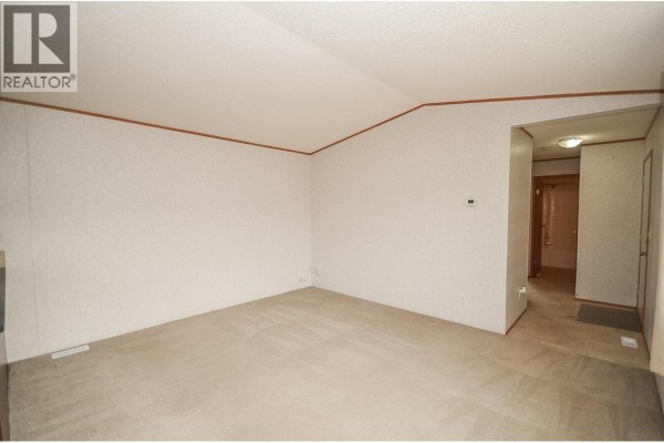 Empty living room with textured white walls, light carpet, and a doorway leading to another room. - 8608 79a Street, Fort St  John