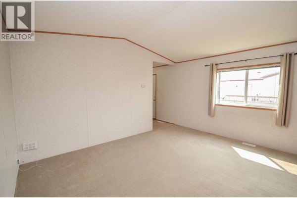 Living room area with light carpet, white textured walls, and a window with beige curtains. - 8608 79a Street, Fort St  John