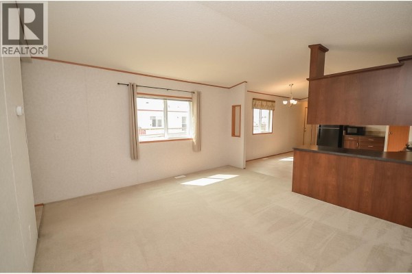 View of the living and dining area, featuring light carpet, white walls, and a dark wood kitchen island. - 8608 79a Street, Fort St  John