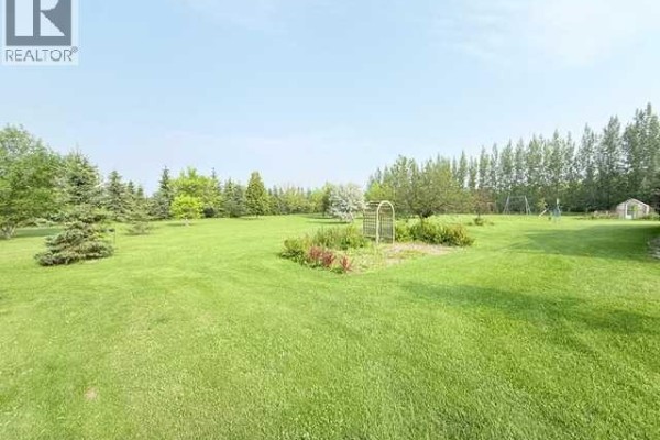 Expansive green lawn with trees, flower beds, an archway, and a distant greenhouse. - 861023 Rr 214, Rural Northern Lights, County Of