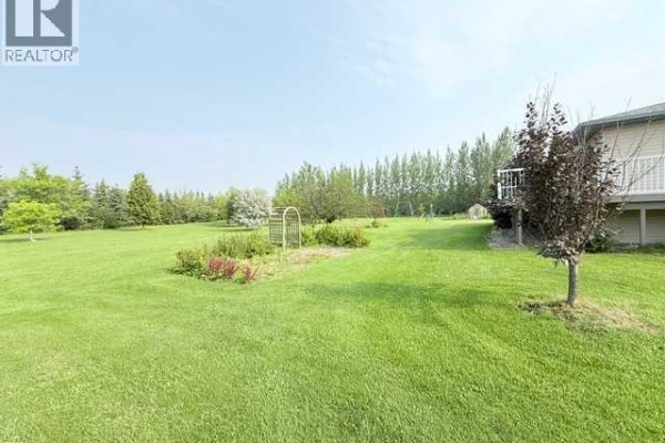 View of the large green lawn, trees, flower beds, and the side of the house with a balcony. - 861023 Rr 214, Rural Northern Lights, County Of