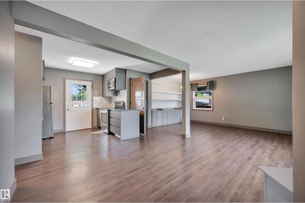 Open-concept living space with a grey kitchen, stainless steel appliances, and laminate flooring. - 8615 66 Av Nw, Edmonton
