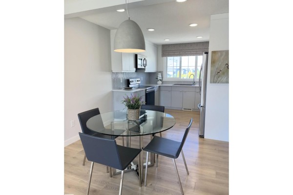 Dining area with a glass table, black chairs, and kitchen in background. - 862 Daniels Wy Sw, Edmonton