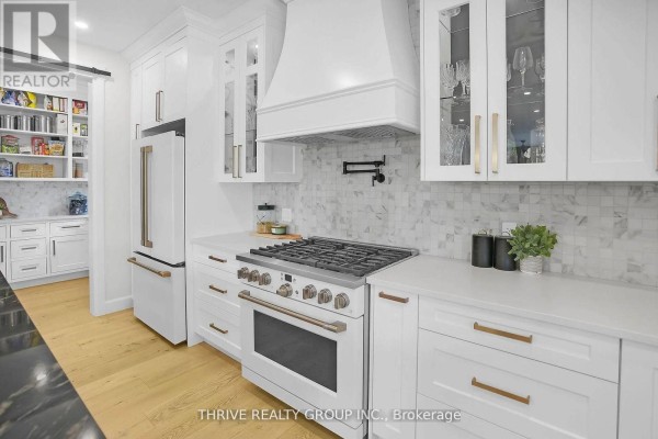 Close-up of a white gas range in a white kitchen with marble backsplash and gold hardware on cabinetry. - 862 Lunar Drive, London North
