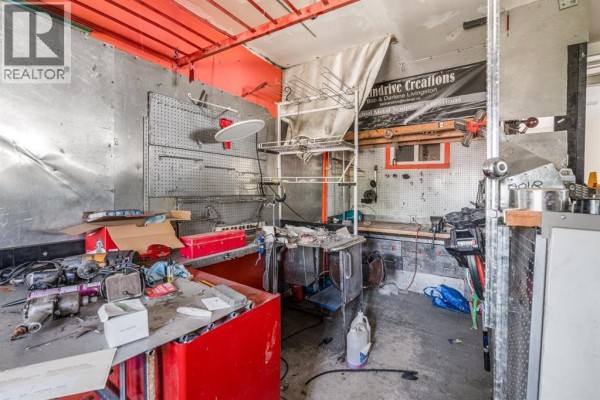 Workshop interior with tool chests, work surfaces, metal walls, and a doorway to another room. - 863 2 Street E, Cardston