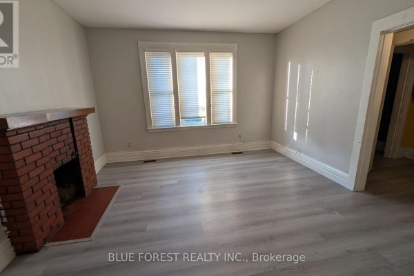 Living room with brick fireplace, pale grey walls, and windows with light filtering through blinds. - 867 Queens Avenue, London East