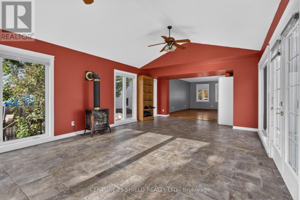 Sunroom with grey tiled floors, red walls, windows, a wood-burning stove, and an open doorway to another room. - 868 Laflin Street, Cornwall