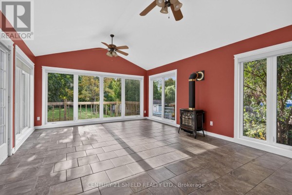 Sunroom with grey tiled floors, red walls, and floor-to-ceiling windows overlooking a backyard deck and trees. - 868 Laflin Street, Cornwall
