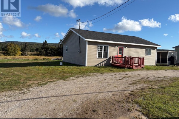 Side exterior view of the bungalow showing the tan siding, red entrance deck, and surrounding green grass. - 86a Main Road, Piccadilly