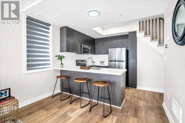 Kitchen with dark wood cabinets, white island with stools, and stainless steel appliances. - 207 - 1555 Kingston Road Pickering On Road, Pickering
