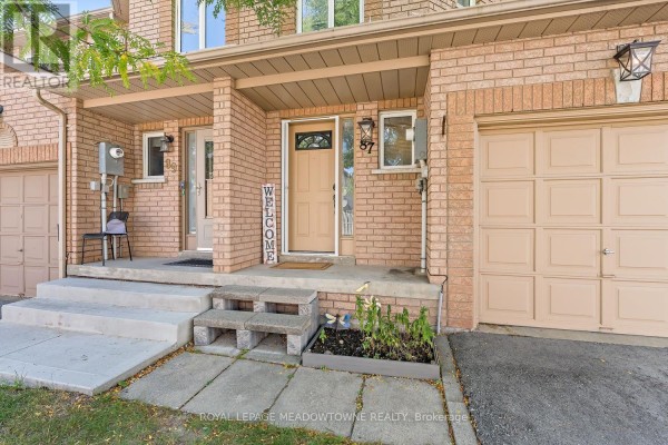 Entrance to townhouse number 87 with light brick, beige garage door, and concrete steps. - 87 - 200 Cresthaven Road, Brampton