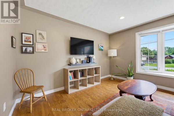Living room with a TV mounted on the wall, shelving unit, chair, and a large window. - 87 Ball Street, Brant