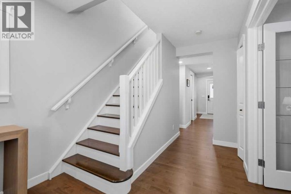Hallway with a staircase featuring white railings and dark wood treads, leading to more doors. - 87 Couture Crescent Sw, Calgary