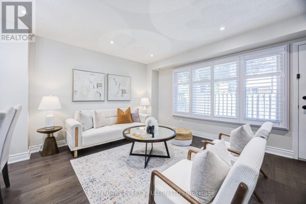 Living room with white sofa, chairs, a patterned rug, and plantation shutters. - 87 Crab Apple Way, Toronto