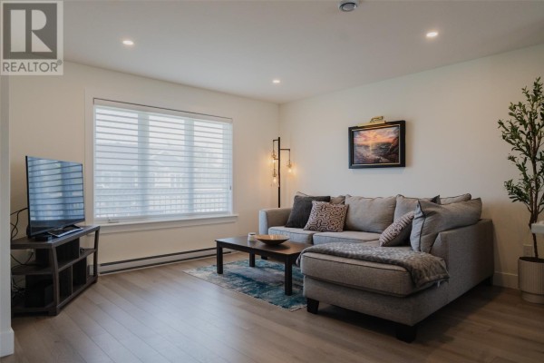 Living room featuring a sectional sofa, coffee table, rug, television on stand, and large window with blinds. - 87 Diamond Marsh Drive, St  John S