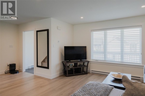 Living room area with a television, window, entryway to stairs, and floor-to-ceiling mirror on the wall. - 87 Diamond Marsh Drive, St  John S