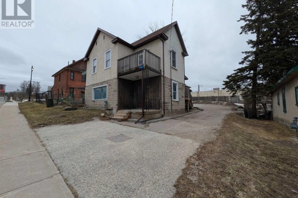Side exterior view of a multi-family home showing the driveway and adjacent properties. - 87 Maple Avenue, Barrie