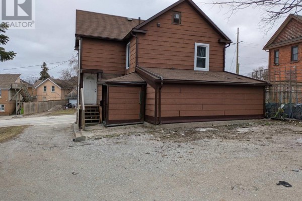 Back view of the multi-family home with gravel driveway and visible snow. - 87 Maple Avenue, Barrie
