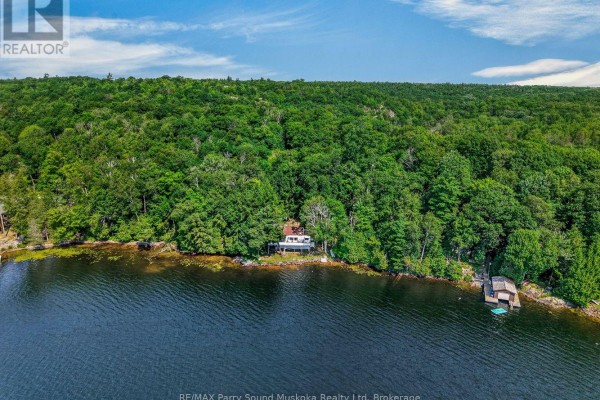 Aerial view of a house on a wooded shoreline with a boathouse on the right. - 87 Millies Road, Seguin