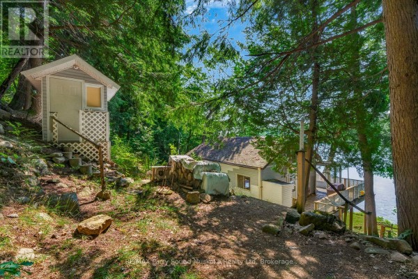 Small utility shed next to a house with firewood stacked on the side, near a lake. - 87 Millies Road, Seguin