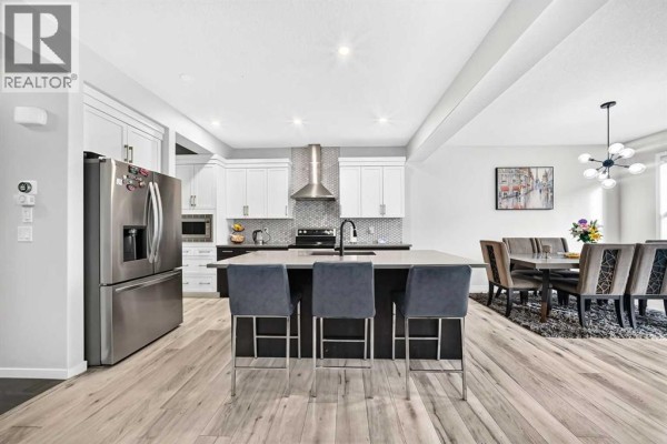 Open concept kitchen with white countertops, dark cabinets, stainless steel appliances, and island seating. - 87 Nolancrest Circle Nw, Calgary