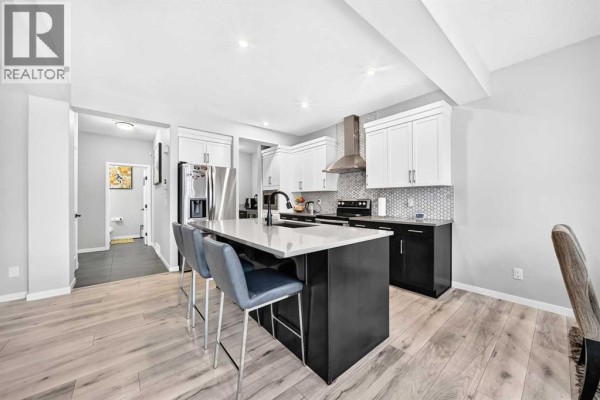 Kitchen with stainless steel refrigerator and oven, white cabinets, and view of a hallway bathroom. - 87 Nolancrest Circle Nw, Calgary