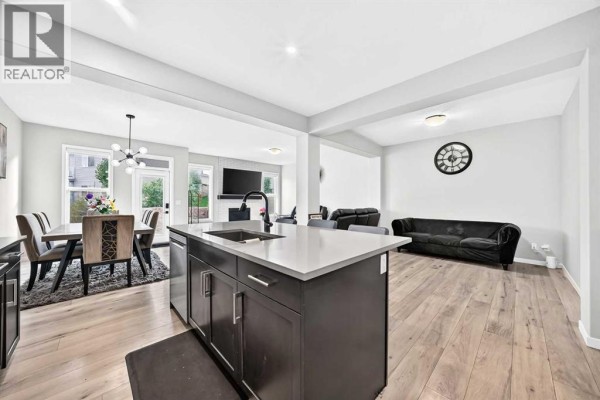 Open concept living and dining area with a fireplace, black leather sofas, and a large dining table. - 87 Nolancrest Circle Nw, Calgary