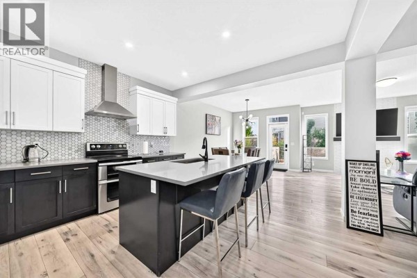 Modern kitchen with a large island, dark cabinets, white uppers, and adjoining dining and living spaces. - 87 Nolancrest Circle Nw, Calgary