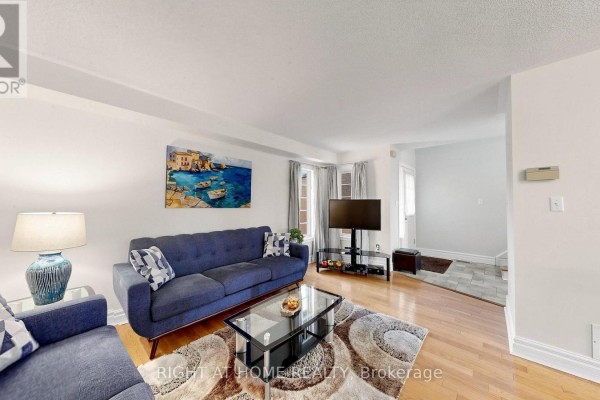 Living room with hardwood floors, blue sofa, coffee table, and television on stand. - 87 Primeau Drive, Aurora