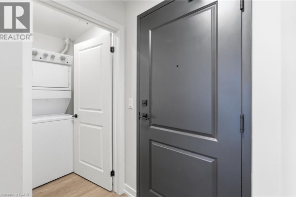 Hallway in an apartment with a dark gray front door and a stacked washer and dryer unit. - 870 Queenston Road Unit# 416, Stoney Creek