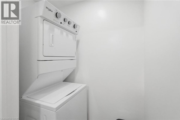 Stacked white Whirlpool washer and dryer unit in a small closet with a white door. - 870 Queenston Road Unit# 416, Stoney Creek