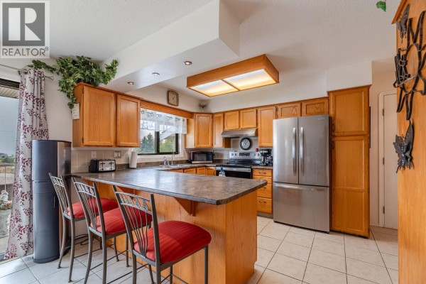 Kitchen featuring oak cabinets, a central island with red stools, and stainless steel appliances. - 8704 Purves Road Unit# 8, Summerland