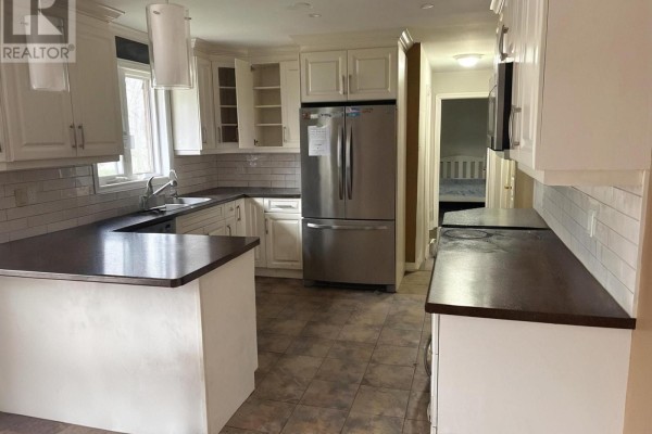 Kitchen with white cabinets, stainless steel appliances, and dark countertops with a view of a hallway. - 8709 8th Line, Essa