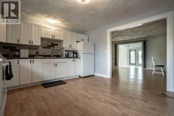 Living room with light green walls, wood-look laminate flooring, and an opening to the kitchen. - 872068 Range Road 235, Rural Northern Lights, County Of